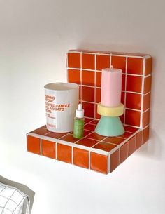 an orange and white tiled shelf with some items on it, next to a cup