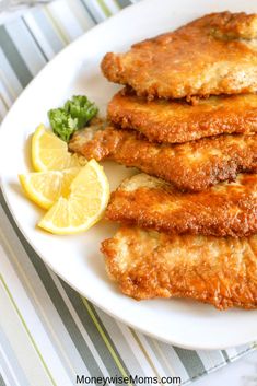 some fried food on a white plate with lemon wedges