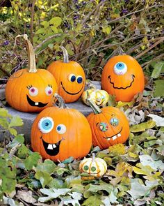 four pumpkins with faces painted on them sitting in the leaves