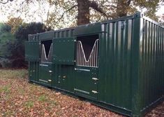 a green shipping container sitting in the middle of a field with trees and leaves around it