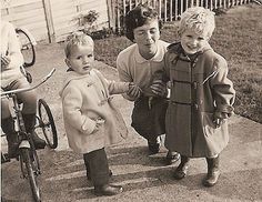 three young children standing next to each other in front of a bicycle and fenced yard