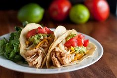 two tacos are sitting on a plate with lettuce and tomatoes in the background