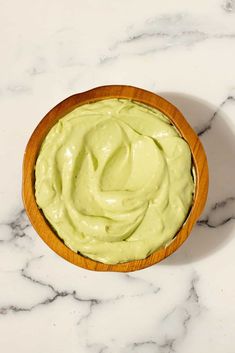 a wooden bowl filled with avocado sitting on top of a white marble counter