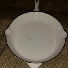 an empty white bowl sitting on top of a brown tablecloth covered floor next to a black and white cat