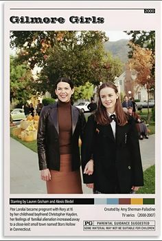 two women standing next to each other in front of a tree and building with autumn colors