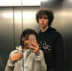 two people standing in front of an elevator taking a selfie with their cell phone