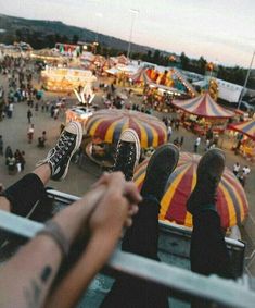 two people sitting on the edge of a carnival looking down at an amusement park filled with rides and fair goers