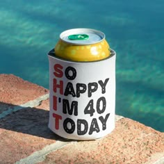 a can cooler sitting on top of a brick wall next to the ocean with an i'm 40 today message painted on it