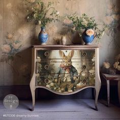 an old dresser with flowers and vases on it in front of a wallpapered background