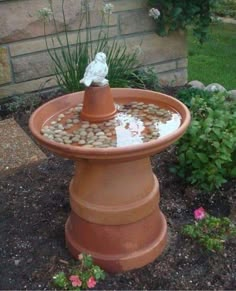 a bird bath in the middle of a garden with rocks and gravel around it's base