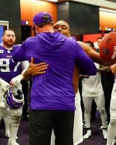 two football players hugging each other in the middle of a room full of people with helmets on