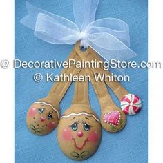 three wooden spoons with painted faces are hanging from a blue ribbon on the wall