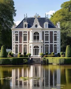 a large white and brown house sitting on top of a lush green field next to a lake