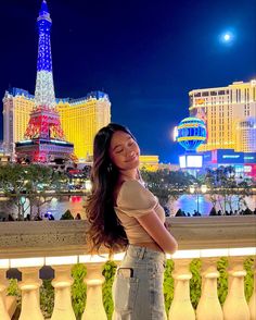 a beautiful young woman standing in front of the eiffel tower and casino at night