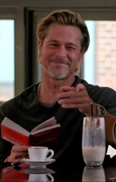 a man sitting at a table in front of a glass of milk and an open book