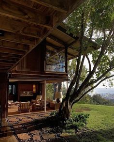 a large tree is in front of a house on the side of a hill with mountains in the background