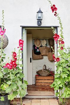 an open door to a white building with flowers and baskets on the outside wall, in front of it