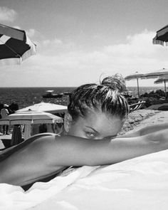 a black and white photo of a woman laying on the beach with umbrellas in the background