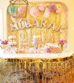 a table topped with lots of cake next to a gold curtain and some pink flowers