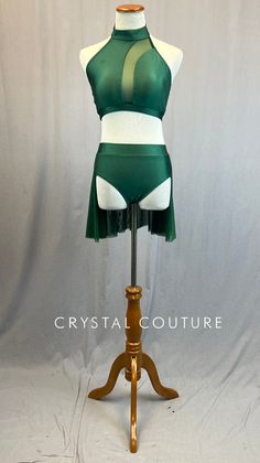 Dark Green mock neck halter top has mesh insert on front of top that curves from left collar bone and down center of sternum. Paired with matching trunks with attached double layer mesh back skirt. *This is a brand new leotard in partnership with Patrick J. We can customize this base to your liking with rhinestones, appliques, skirts, feathers, etc. **Costume in image is an AS, Photographed on an AS/AM Mannequin with Measurements of: Bust 35", Ribcage 30", Waist 25", Hip 34", Girth 57" Fitted Sheer Mesh Skirt, Sheer Fitted Mesh Skirt, Fitted Green Bottoms For Dance, Neck Halter Top, Green Two Piece, Back Skirt, Collar Bone, Rib Cage, Leotards