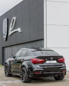 a black bmw car parked in front of a building with the logo on it's side