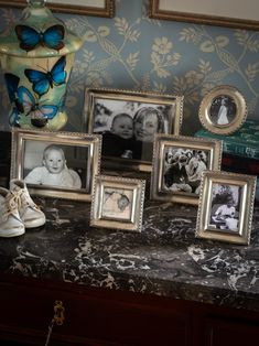 a table topped with framed pictures and baby shoes next to a vase filled with flowers