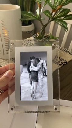 a person holding up a photo in front of a table with a potted plant