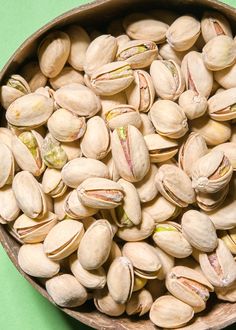 a bowl filled with pistachios on top of a green surface