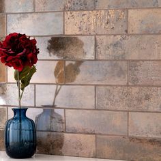 a blue vase with a red rose in it on a counter top next to a brick wall