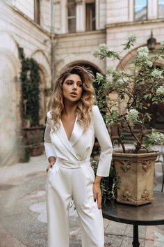 a woman standing in front of a potted plant wearing a white suit and heels