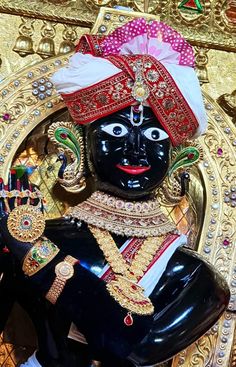 a black statue with gold and red designs on it's face, surrounded by other decorations