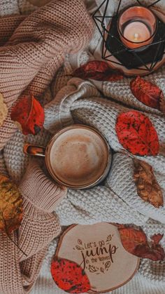 a cup of coffee sitting on top of a blanket next to a candle and some leaves