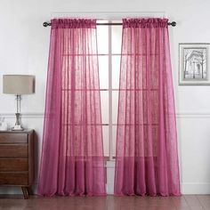 a pink curtain hanging on the side of a window next to a dresser and lamp