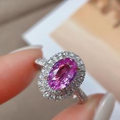 a close up of a person's hand holding a ring with a pink stone