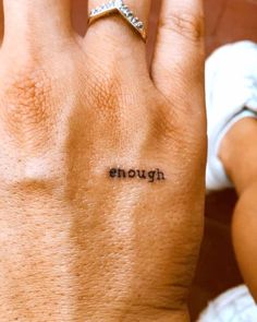 a woman's left hand with the word enough tattooed on her right thumb and finger