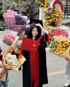 a woman in graduation gown holding bouquets of flowers