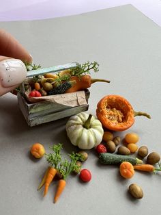 a person is holding a knife over some miniature vegetables and fruits on a counter top