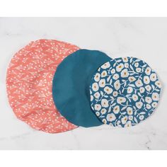 three round placemats in various patterns on a white marble surface with blue and orange circles