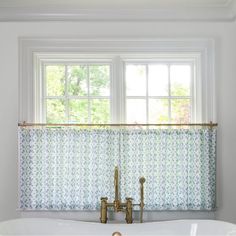 a bath tub sitting under a window next to a faucet in a bathroom