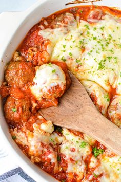 a wooden spoon in a white casserole dish filled with meatballs and cheese