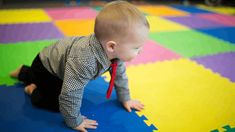 a baby wearing a tie crawling on the floor in a play room with colorful tiles