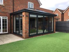 a brick building with glass walls and sliding doors on the outside, next to a green lawn