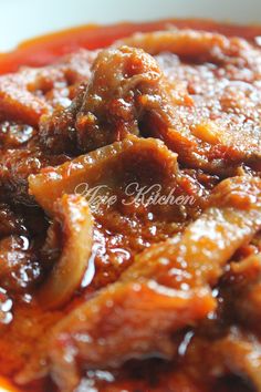 a bowl filled with meat and sauce on top of a wooden table next to a white plate