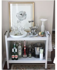 a white shelf with bottles and glasses on it in front of a framed photograph,