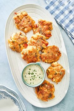 a white plate topped with crab cakes next to a small bowl of ranch dressing on a blue table cloth