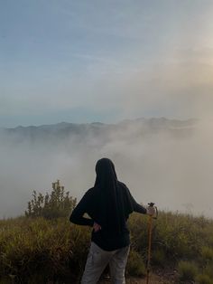 a person standing on top of a hill with a stick in their hand and fog behind them