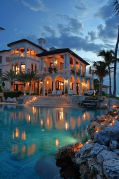 a large house with a pool in front of it at night, surrounded by palm trees