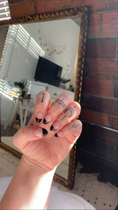 a woman's hand with black and white nail designs on it, in front of a mirror