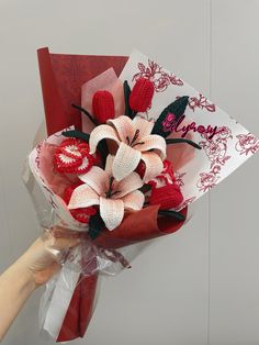 a hand holding a red and white paper bouquet with flowers on it's side