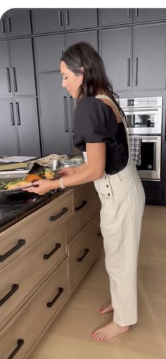 a woman standing in front of an oven with her hand on the stovetop and looking at something